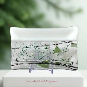 May include: A rectangular glass soap dish with a white top and a clear base. The base is decorated with green speckles, green triangles, and black lines. The dish is supported by a clear plastic stand. The text "SoapAndDish.Etsy.com" is visible.