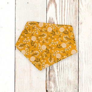 May include: A yellow bandana with a white floral pattern. The bandana is made of fabric and has a triangular shape.