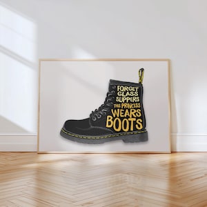 Puede incluir: Impresión enmarcada de una bota negra con costuras y detalles amarillos. El texto en la bota dice: "Olvídate de los zapatos de cristal, esta princesa usa botas". La obra de arte se muestra sobre un fondo blanco.