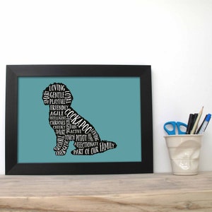 Può includere: Una stampa incorniciata di una silhouette nera di un cane Cockapoo con le parole "Loving, Gentle, Playful, Friendly, Agile, Intelligent, Curious, Cheeky, Fun, Smart, Active, Couch Potato, Affectionate, Part of Our Family" scritte all'interno della silhouette su uno sfondo blu-verde.