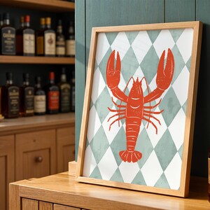 Può includere: Una stampa artistica incorniciata con un'illustrazione di aragosta rossa su uno sfondo a motivo di diamanti bianchi e verde acqua. La stampa è esposta su una superficie di legno, con una credenza di liquori sullo sfondo.