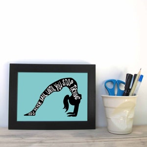 Könnte beinhalten: Ein schwarzer gerahmter Druck mit hellblauem Hintergrund. Der Druck zeigt eine Silhouette einer Person, die eine Yoga-Pose macht, mit dem Text "You never fail until you stop trying", der um die Silhouette geschrieben ist.