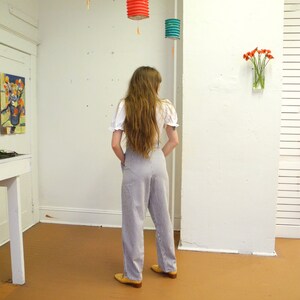 May include: A person wearing a white blouse and blue and white striped pants. The person is standing in a room with a white wall and a wooden floor. There are three paper lanterns hanging from the ceiling.