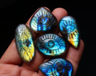 May include: Five iridescent labradorite gemstone pendants with carved eye designs. The pendants are in various shapes and sizes, with a blue and yellow colour scheme.