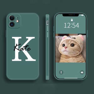May include: A teal phone case with the letter "K" and the name "Kate" in white. The phone screen displays a cat wearing a bear hat. The time on the screen reads 12:54.