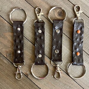 May include: Four brown leather keychains with silver key rings and clasps. Each keychain has a different design of small metal studs.
