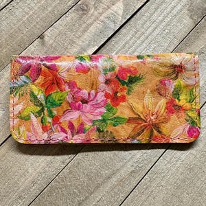 May include: A rectangular floral print case featuring a vibrant array of pink, red, yellow, and green flowers. The case has a tan background and is stitched with pink thread. The case is likely made of leather or a similar material.