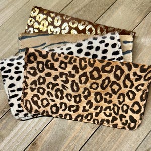 Puede incluir: Cuatro carteras de cuero con estampado de animales. Las carteras son todas del mismo tamaño y forma, pero tienen diferentes patrones. Los patrones incluyen estampado de leopardo, estampado de guepardo y estampado de cebra.