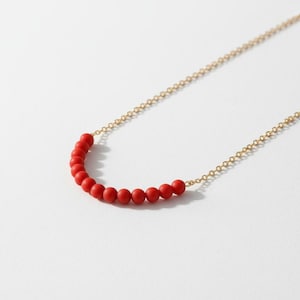 May include: A delicate necklace featuring a strand of small, vibrant red beads. The beads are strung along a fine, gold-colored chain. The necklace is displayed on a white background, highlighting the contrast between the colors.