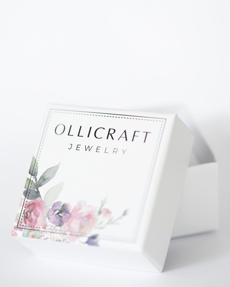 May include: White jewelry box with the text "OLLICRAFT JEWELRY" in silver lettering. The box features a floral design with pink, purple, and green watercolor flowers. The box is slightly open, revealing the inside.