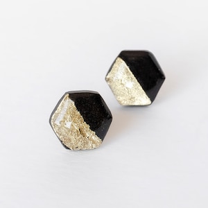 Könnte beinhalten: Ein Paar schwarze und goldene sechseckige Ohrstecker. Jeder Ohrstecker ist halb schwarz und halb gold, wobei der goldene Teil eine strukturierte, metallische Oberfläche hat.