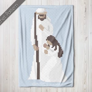 Può includere: Uno schema di uncinetto che presenta una coperta bianca con una rappresentazione di un uomo e una ragazza in vesti bianche. L'uomo tiene un bastone e la ragazza tiene le mani giunte in preghiera.