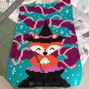 May include: A colorful crochet pattern featuring a whimsical fox dressed as a witch. The fox has orange fur, a black hat, and is set against a teal background with purple and pink accents. The words "Crochet Pattern" are in the upper left corner.