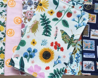 Puede incluir: Seis paneles de tela con diferentes patrones. Los paneles son blancos con varios diseños florales y geométricos. Un panel tiene un fondo azul con sellos de todo el mundo. Los paneles están todos alineados en una fila.