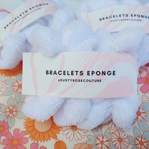 Puede incluir: Scrunchies blancos y esponjosos con una etiqueta rosa y blanca que dice "Bracelets Eponge @dustyrosecouture".