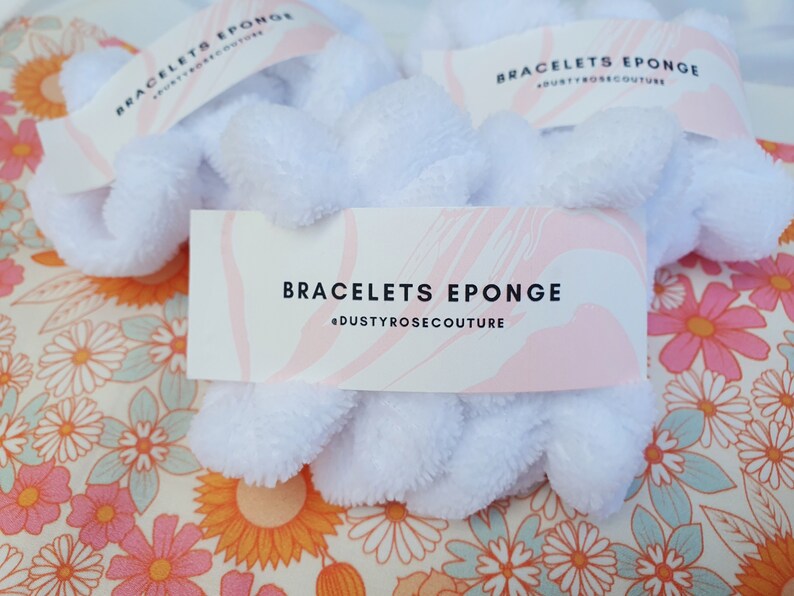 Puede incluir: Scrunchies blancos y esponjosos con una etiqueta rosa y blanca que dice "Bracelets Eponge @dustyrosecouture".