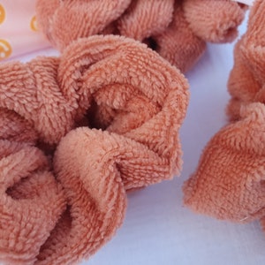 Puede incluir: Tres scrunchies marrones y peludos. Los scrunchies est&aacute;n hechos de una tela suave y peluda.