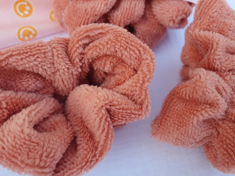 Puede incluir: Tres scrunchies marrones y peludos. Los scrunchies est&aacute;n hechos de una tela suave y peluda.