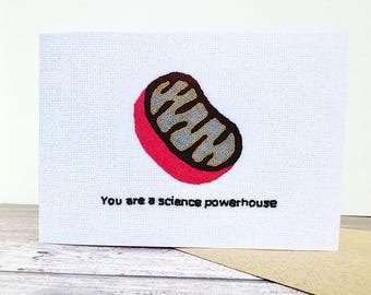 Op de afbeelding: Een witte kaart met een rode en zwarte illustratie van een mitochondrium, een celorganel. De tekst "You are a science powerhouse" is onder de illustratie gedrukt.