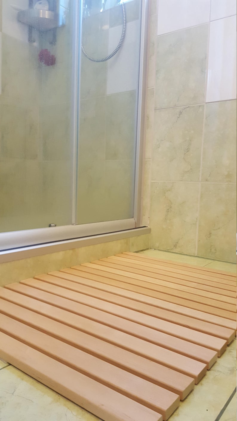 May include: A wooden bath mat with slats made of light brown wood. The mat is placed on a tiled floor in a bathroom.