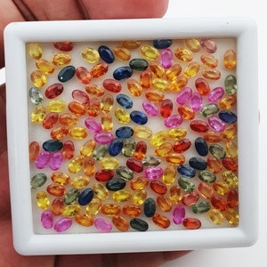 Op de afbeelding: Een verzameling ovale edelstenen in verschillende kleuren, waaronder rood, oranje, geel, groen, blauw en paars. De edelstenen zijn gerangschikt in een witte schaal.