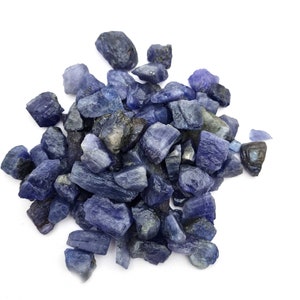 Op de afbeelding: Een hoop ruwe, blauw-paarse edelstenen. De stenen zijn van verschillende groottes en vormen, sommige hebben een meer puntige of grillige vorm.