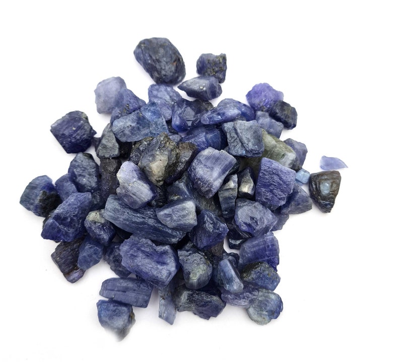 Op de afbeelding: Een hoop ruwe, blauw-paarse edelstenen. De stenen zijn van verschillende groottes en vormen, sommige hebben een meer puntige of grillige vorm.