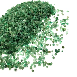 May include: A large pile of small, green emerald gemstones. The emeralds are of various shapes and sizes, and some are tumbled.