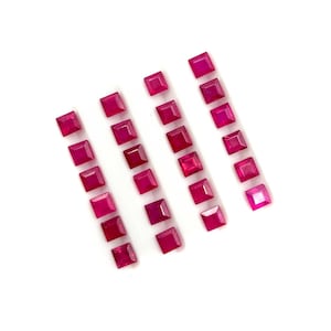 May include: A collection of twenty-one square-cut, vibrant pinkish-red gemstones arranged in four vertical rows. Each gemstone features a faceted surface that reflects light, showcasing a consistent deep magenta hue and a uniform square shape.