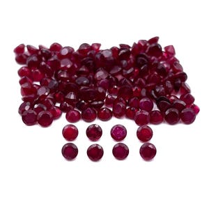 May include: A large pile of loose red ruby gemstones, with a smaller group of 10 red ruby gemstones arranged in a row below.