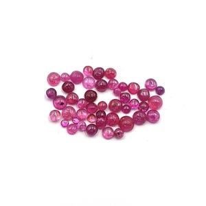 May include: A collection of loose, round, polished beads in various shades of vibrant pink and magenta. These small, spherical items feature smooth, glossy surfaces and varying sizes, scattered together to display their translucent colour tones.