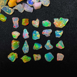 May include: A collection of raw opal gemstones, displaying a variety of shapes and colors. The opals exhibit a play of color with flashes of green, red, and blue. The gemstones are set against a dark background.