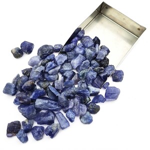 Op de afbeelding: Een grote stapel ruwe, blauwe edelstenen, waarvan sommige in een metalen bakje liggen. De edelstenen zijn van verschillende groottes en vormen.