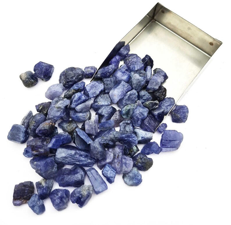 Op de afbeelding: Een grote stapel ruwe, blauwe edelstenen, waarvan sommige in een metalen bakje liggen. De edelstenen zijn van verschillende groottes en vormen.