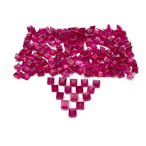 Könnte beinhalten: Eine große Ansammlung kleiner, quadratisch geschliffener, leuchtend pink-roter Edelsteine, die oben in einer dichten Gruppe angeordnet sind, mit einer kleineren, geordneten dreieckigen Formation einzelner quadratischer Steine darunter.
