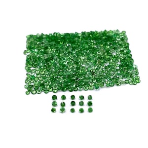 May include: A large collection of small, round, faceted green gemstones arranged in a rectangular cluster, with fifteen individual stones placed in three neat rows of five below the main group, all displaying a vibrant emerald green hue.