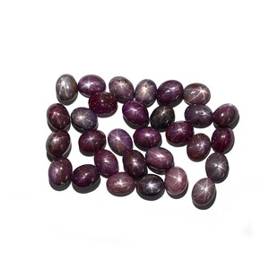 May include: A collection of 20 oval-shaped, purple star sapphires. The sapphires have a star-like pattern in the center of each stone.