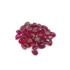May include: A pile of pear-shaped red gemstones, likely rubies, on a white background.