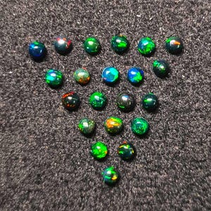 以下が含まれることがあります： 暗いベースカラーの、小さくて丸いオパールのコレクション。 オパールは、緑、青、オレンジなど、さまざまな鮮やかな色を示し、きらめく効果を生み出しています。 オパールは、暗く質感のある表面に配置されています。