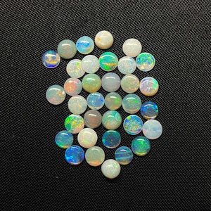 May include: A selection of polished, circular opals in a range of colours, including white, blue, green, and orange. The opals are arranged on a black surface, highlighting their iridescent play-of-colour. These gemstones are suitable for jewellery making.