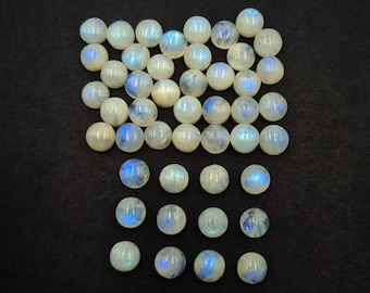 Op de afbeelding: Een verzameling ronde, gepolijste maansteen cabochons. De stenen zijn overwegend wit met iriserende blauwe flitsen, gerangschikt op een donkere achtergrond. Deze edelstenen zijn ideaal voor het maken van sieraden.