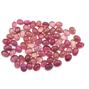 Peut inclure: Une collection de pierres précieuses ovales dans des tons de rose et de rouge. Les pierres précieuses sont dispersées sur une surface blanche, avec un mélange de teintes claires et foncées. Les pierres polies ont un aspect lisse et brillant.