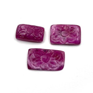 Op de afbeelding: Drie roze gegraveerde edelsteen cabochons met een bloemmotief. De cabochons zijn rechthoekig en hebben een glad, gepolijst oppervlak.