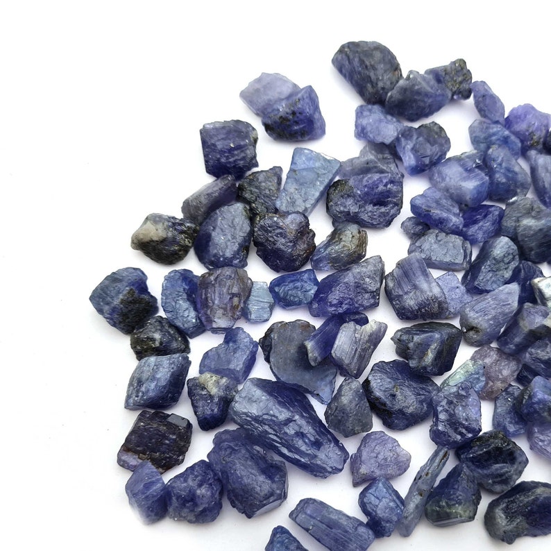 Op de afbeelding: Een verzameling ruwe, blauw-paarse edelsteenkristallen. De kristallen zijn in verschillende vormen en maten, sommige zijn lang en dun, terwijl andere ronder zijn.
