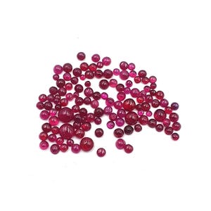 May include: A collection of numerous small, round, cabochon-cut gemstones in varying shades of deep pink and vibrant red. These polished, smooth, and translucent stones are scattered across the frame, displaying a range of sizes and intensities.