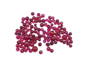 May include: A collection of numerous small, round, cabochon-cut gemstones in varying shades of deep pink and vibrant red. These polished, smooth, and translucent stones are scattered across the frame, displaying a range of sizes and intensities.