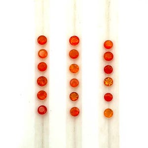 Puede incluir: Filas de pequeñas gemas redondas y naranjas. Las gemas varían en tonalidad, desde un rojo-naranja brillante hasta un tono más claro, amarillo-naranja. Las gemas están dispuestas en líneas verticales sobre un fondo blanco.