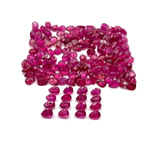 May include: A collection of numerous small, faceted, pear-shaped rubies in a vibrant deep pinkish-red hue. The gemstones are arranged in a large, dense cluster at the top, with sixteen individual stones organized in four neat rows below.