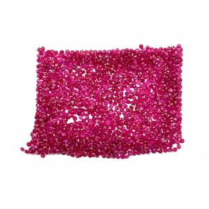 Pode incluir: Uma coleção de pequenas pedras preciosas facetadas, vermelho escuro, possivelmente rubis, dispostas em forma retangular sobre um fundo branco. As pedras preciosas são densamente compactadas, criando uma aparência vibrante e texturizada.