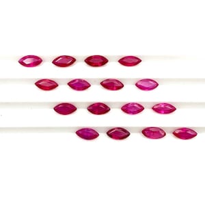 May include: A collection of fifteen loose marquise-cut rubies arranged in four horizontal rows. Each gemstone features a vibrant, deep red color with a faceted surface that reflects light, showcasing a pointed oval shape on a white surface.